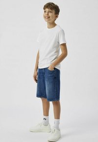 Balti medvilninė marškinėliai, mėlyni džinsiniai šortai, balti sportbačiai ir baltos kojinės su juodomis detalėmis. Paprastas, kasdienis ir patogus dizainas.