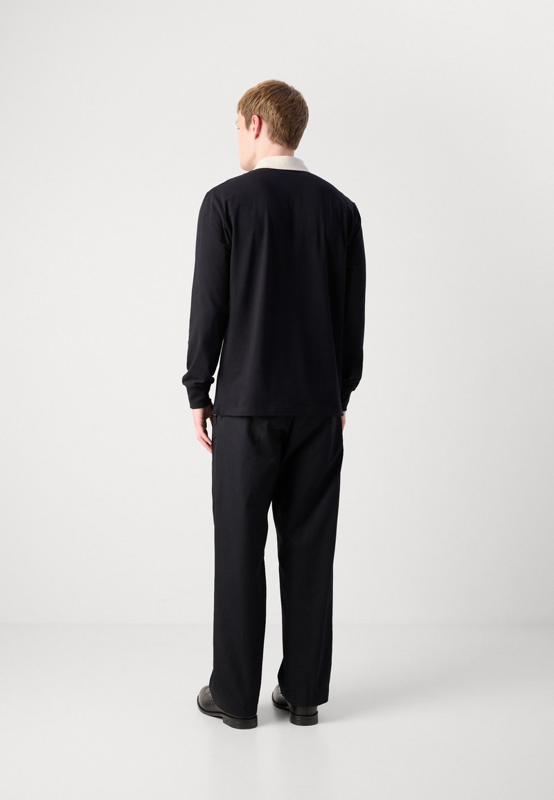 Zwarte longsleeve shirt met een witte kraag, gecombineerd met losse zwarte broeken. De stof lijkt soepel, met een ontspannen pasvorm en een minimalistisch ontwerp.