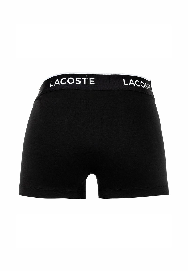Schwarze Baumwoll-Boxershorts mit einem breiten, elastischen Bund, auf dem "LACOSTE" in Weiß gedruckt ist. Glatte Textur und schmal geschnittenes Design.