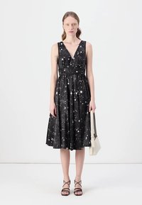 Black sleeveless dress with a V-neck, star pattern, belted waist, and flared skirt. Paired with strappy black shoes and a white handbag.