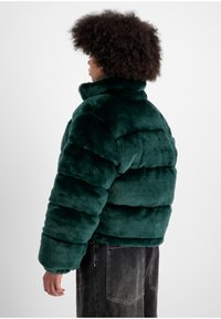 Geacă puffer din blană sintetică de culoare verde închis, cu guler înalt și design îmblănit. Manșete elastice și o croială lejeră, potrivită pentru purtarea casual.