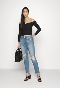 Top preto às riscas, de mangas longas e ombros à mostra, jeans rasgados azul claro, mala preta e saltos altos pretos. Tecido suave, ajuste casual.