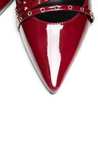 Scarpa con tacco alto in pelle verniciata rossa, con punta a forma appuntita, caratterizzata da cinturini incrociati con dettagli in metallo dorato.