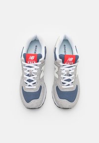 Zapatillas New Balance 574 en gris y marino con parte superior de ante y malla, cordones blancos y una etiqueta roja con el logotipo y el número de modelo.