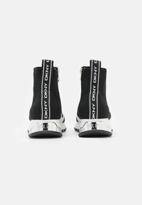 Czarne dzianinowe botki do kostki z zamkiem błyskawicznym, z odblaskowym srebrnym obcasem i białym logo na plecach dla dodatkowego efektu.