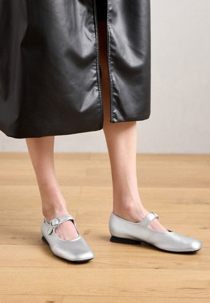 Sidabrinės odinės baletinės bateliai su apvaliu pirštu ir sagtimi, turinčios žemą kulną ir lygų, blizgų paviršių.