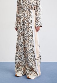 Leopardmönstrade byxor i beige och svart, med elastisk midja, vita sidostripes och märkta accenter. Tillverkade av mjukt, flödande tyg.