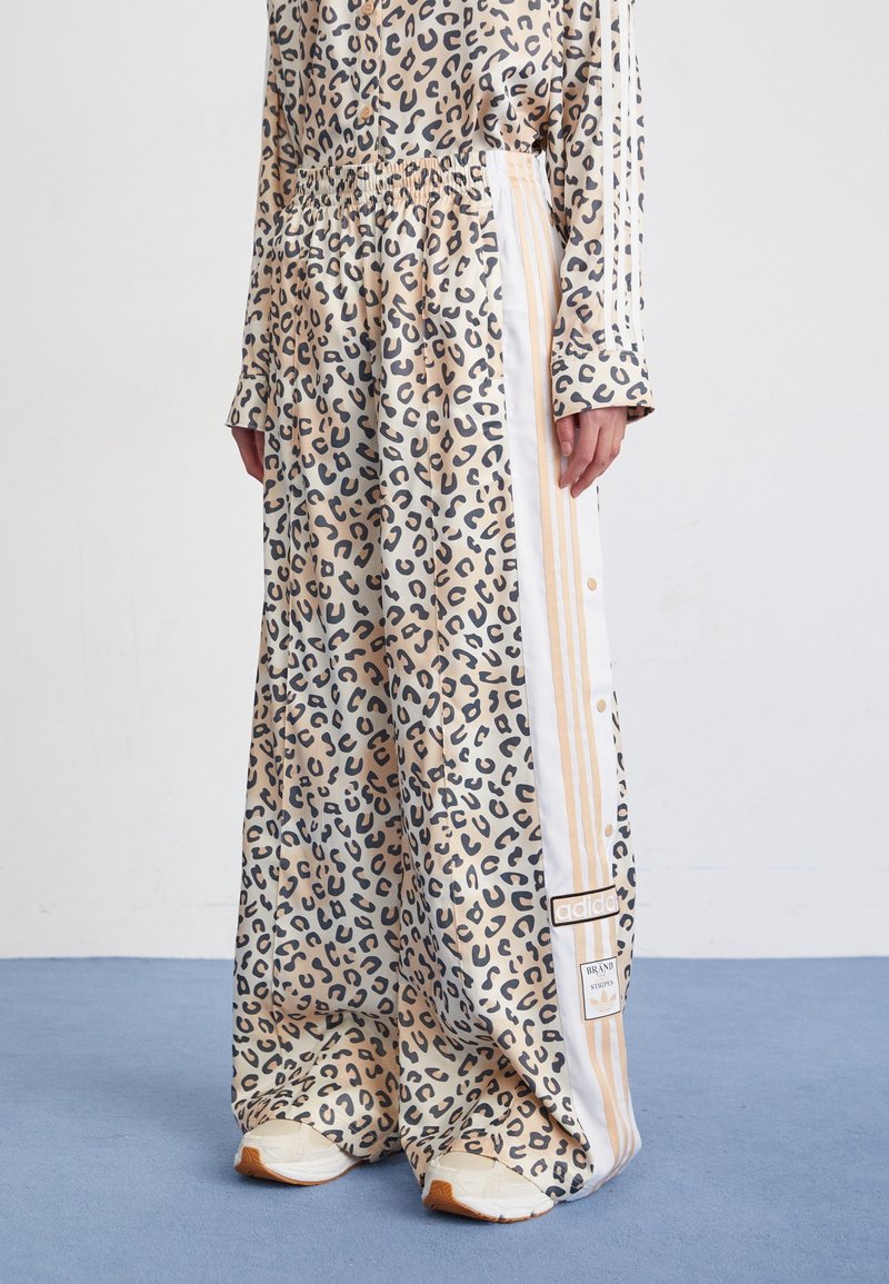 Leopardmönstrade byxor i beige och svart, med elastisk midja, vita sidostripes och märkta accenter. Tillverkade av mjukt, flödande tyg.