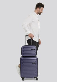 Set di valigie rigide viola con design a strisce orizzontali. Include un bagaglio a mano e una valigia espandibile. Entrambi presentano dettagli neri e ruote.