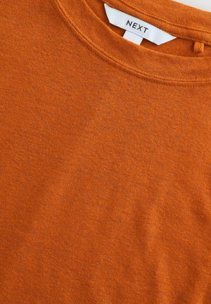 Korte mouwen, oranje T-shirt van zacht katoen. Heeft een ronde hals en een label met "NEXT" aan de achterkant van de halslijn. Getextureerde stof.