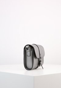 Borsa in pelle grigia con una forma arrotondata, chiusura a patta e tracolla regolabile. Tra gli accessori spiccano un gancio metallico e un dettaglio ad anello.
