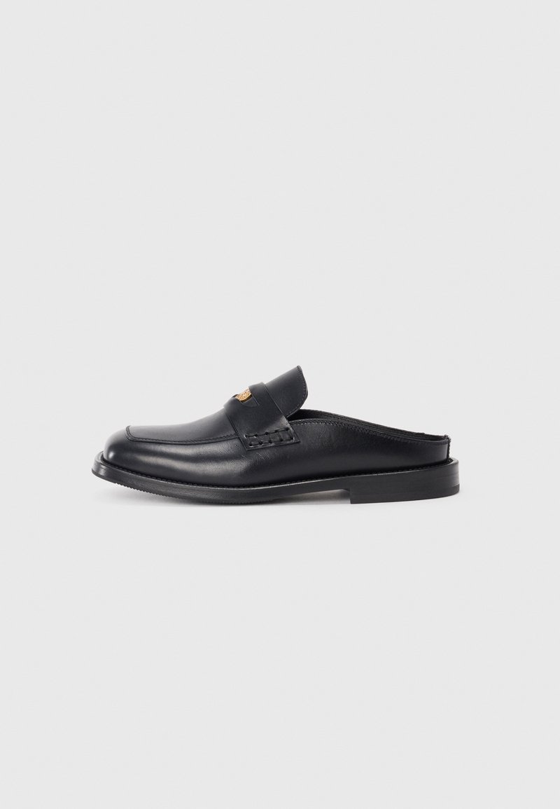 Black leather slip-on shoe with a rounded toe, low heel, and woven design detail on the upper. Features minimalistic styling and smooth texture.