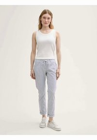 Biała koszulka na ramiączkach w połączeniu z jasnoniebiesko-białymi spodniami w paski, z talią na sznurek, mankietami na nogawkach oraz białymi trampkami.