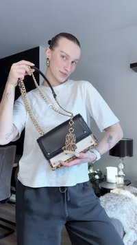 Črna usnjena torbica z zlatim verižnim trakom, poudarki z leopardjim vzorcem in kontrastnim belim panelom. Ima čepke in okrasno oznako.