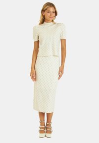 Biały zestaw składający się z dwóch części, z teksturowanym, dzianinowym topem z krótkimi rękawami oraz dopasowaną spódnicą o średniej długości. Całość dopełniają białe sandały na obcasie.