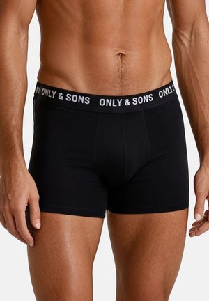 Mannelijke torso met zwarte boxershorts met "ONLY & SONS" merkband, staand tegen een effen lichte achtergrond.