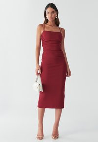 Bordó přiléhavé šaty s tenkými ramínky, nařasenými detaily a midi délkou. Doplněné bílou kabelkou a béžovými střevíci na pásky.