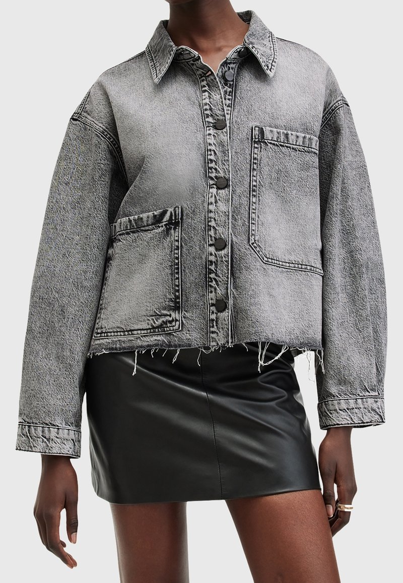 Grijze denim cropped jas met twee voorzakken, knoopsluitingen en rafelige zoom. Gedragen over een zwarte leren minirok.