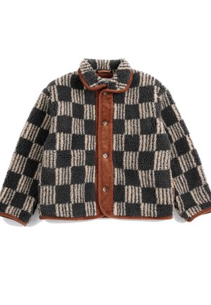 Enfant aux cheveux roux bouclés portant un bonnet rouge en tricot et une veste polaire noire et beige à carreaux, boutonnée, avec une bordure en velours côtelé marron.
