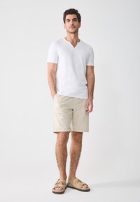 White short-sleeve V-neck t-shirt, light beige shorts, and tan sandals. Features a casual fit and soft texture.