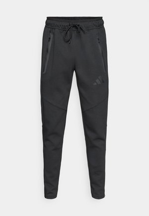 Μαύρα αθλητικά παντελόνια τζόγκινγκ με ελαστική μέση και κορδόνι, δύο τσέπες με φερμουάρ στα πλαϊνά και διακριτικά λογότυπα. Κατασκευασμένα από μαλακό, υφασμένο υλικό.