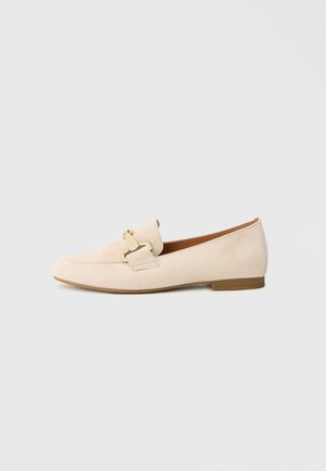 Beige Wildleder-Slipper mit flacher Sohle, versehen mit einer goldfarbenen Schnallendetail vorne und abgesteppten Akzenten entlang der Nähte.