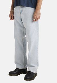 Lichtblauwe denim jeans met een losse pasvorm, recht model en contrasterende stiksels, gecombineerd met zwarte enkellaarzen.