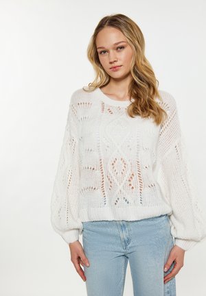 Pulover alb tricotat cu modele brodate, mâneci tip balon și tiv ribat, asortat cu blugi deschiși la culoare. Design texturat și aerisit.