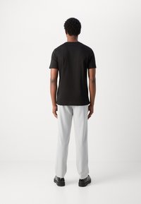 Black short-sleeve t-shirt, slim fit, paired with light gray pants and black shoes, viewed from the back against a plain white background.