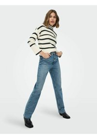 Prugasti džemper u krem i crnoj boji s visokim ovratnikom; kombiniran s plavim trapericama ravnog kroja; uz crne gležnjače.