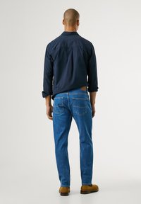 Tengerészeti hosszúujjú ing, kék farmernadrág és világosbarna velúr cipők. Az ing gombos gallérral rendelkezik, a farmernadrág pedig klasszikus öt zsebes dizájnnal készült.