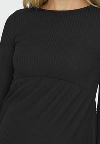 Black ribbed long-sleeve top featuring a rounded neckline and a fitted bodice that flares out at the waist, highlighting texture and design.
