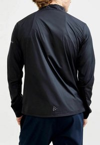 Schwarze, leichte, langärmelige Sportjacke mit hohem Kragen und strukturiertem Stoff. Verfügt über ein kleines Logo auf der linken Schulter und im Rücken.
