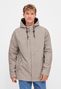 Beige water-resistant jacket with a hood, contrasting black drawstrings, front zip pocket, and side pockets. Smooth texture and casual fit.