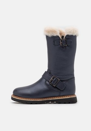 Botte mi-mollet en cuir bleu marine avec doublure en peau de mouton beige, deux boucles métalliques réglables, et une semelle en caoutchouc noire avec coutures beiges.