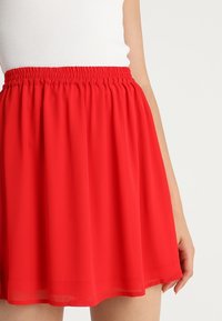 Roter, leichter Rock aus Stoff mit einem elastischen Bund, der ein fließendes Design und eine glatte Textur aufweist, knielang und ohne sichtbare Muster.