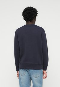 Marineblå hettegenser, rund hals, ribbestrikkede mansjetter og kant, laget av mykt, teksturert stoff, kombinert med lyseblå jeans.