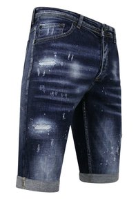 Dongenhorts in een donkere wassing met distressed details, zichtbaar verfbossen en opgerolde boorden. Voorzien van standaardsakken en knoopsluiting.