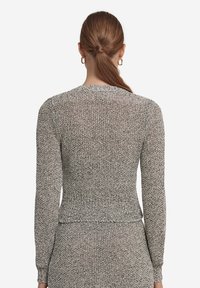 Grå och krämfärgad strukturerad stickad tröja med långa ärmar, figurnära midja och ribbade detaljer vid ärmslut och fåll. Bakifrån syns ett subtilt mönster.