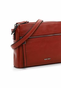 Red leather crossbody bag with a smooth texture, featuring a zippered closure, an adjustable strap, and a metallic brand logo.
