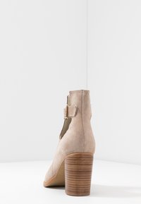 Bottine beige en daim avec talon bloc en bois empilé et détail boucle latérale, vue de dos sur fond blanc.