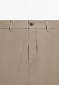 Beige Hosen mit glatter Textur, schmaler Passform, mit Knopfverschluss, schräge Taschen und dezenten Nähdetails.