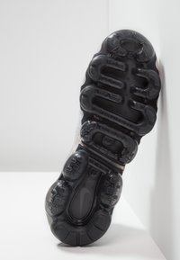 Schoenenzool met een gestructureerd zwart rubberen oppervlak, met cirkelvormige en ovale padding, en een zichtbaar logo in het midden.