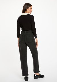 Suéter negro con un cuello crema, combinado con pantalones vaqueros oscuros de tiro alto y corte holgado, y zapatos negros de plataforma.