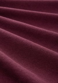 Tessuto borgogna con una consistenza liscia e un leggero motivo a coste, che mostra pieghe delicate e una struttura a maglia uniforme.