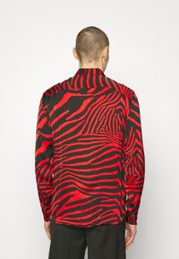 Maglietta nera con motivo a strisce zebrate rosse, con colletto, maniche lunghe e spacchi laterali. Tessuto dalla texture liscia.