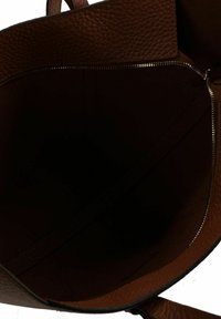 Interno di borsa in pelle marrone texturizzata con cerniera e bordi lisci, caratterizzato da un ampio scomparto non foderato.