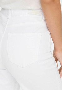 Vaqueros de denim blanco que presentan un bolsillo trasero con forma triangular. La textura es suave y la costura es sutilmente visible.