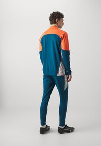 Sportkleding met een kleurblokontwerp in teal, oranje en een gestreepte zijpaneel; gemaakt van lichtgewicht, rekbaar materiaal.