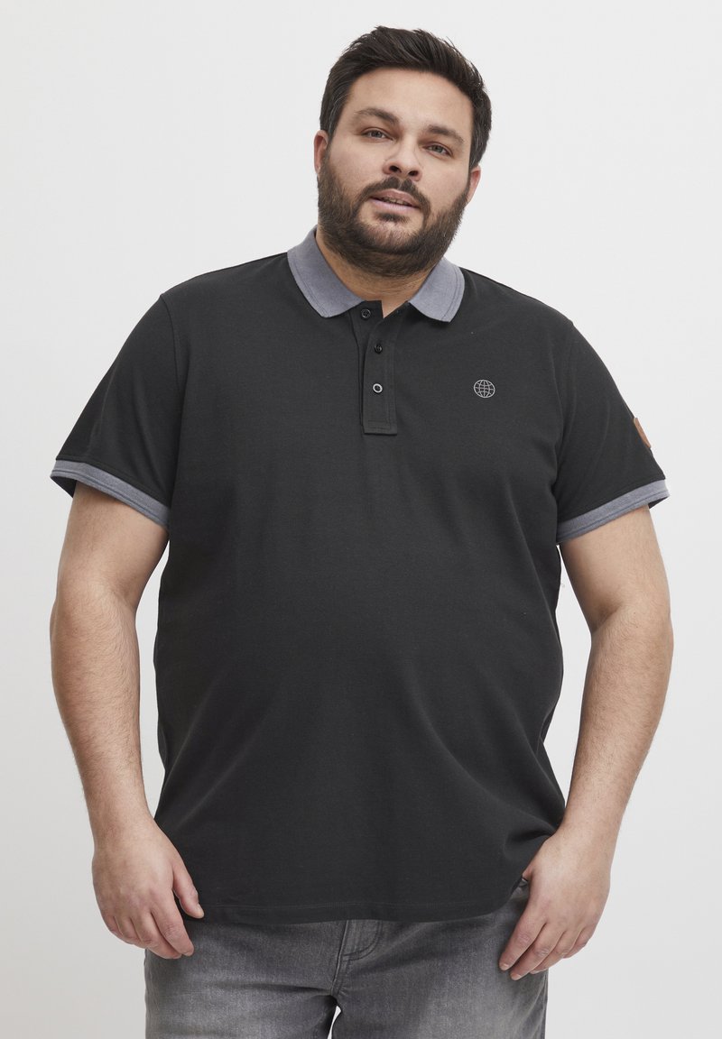 Svart polo skjorte med grå krage og ermeakenter, med en liten logo på brystet og to svarte knapper for lukking.